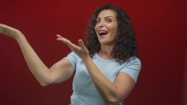 Kadın avuçlarını geniş bir gülümseme ile canlı kırmızı stüdyo duvarına karşı açar anlamlı bir jest göstererek; mutluluk.
