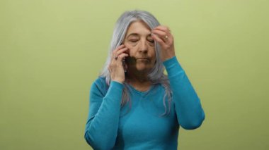 Hüsrana uğramış bir ifadeyle telefonda konuşan bir kadın canlı sarı bir arka plana karşı, mavi bir kazak giyiyor, stres ve iletişim sorunları tasvir ediyor..