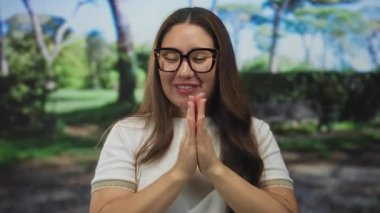 Kadın güneş parkında yüzüne yakın el kaldırır gözlük ve beyaz gömlek giyerek geniş bir gülümseme içinde; mutluluk neşe sevinç memnuniyeti.