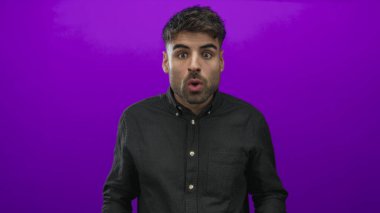 Siyah gömlek giyerken mor stüdyo arkaplanı karşısında şaşırmış gözlerle gözlerini ovuşturan genç İspanyol adam..