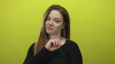 Yeşil stüdyo duvarına karşı yumruğunu kameraya doğru uzatan sırıtan beyaz bir kadın..