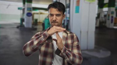 Genç İspanyol bir adam bir benzin istasyonunda ekose gömlek ve ciddi bir ifade takınarak mola veriyor..