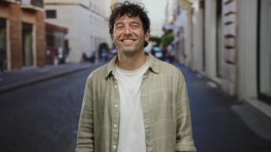 İspanyol bir adam gülümsüyor ve büyüleyici bir sokakta öpüşüyor. Sıradan ve keyifli bir an, şehir ortamında yakışıklı tarzını vurguluyor..