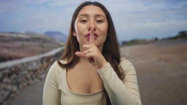 Gündüz vakti sessiz kalmak için parmakları dudaklarına kadar dudaklarına değen genç İspanyol kadın parmak hareketi ve tarafsız ifade gösteriyor..