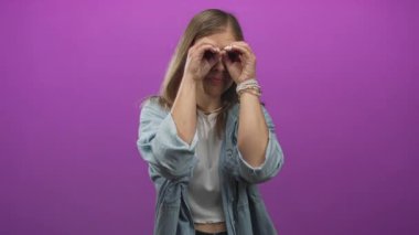 Sarışın genç bir kadın parlak bir stüdyo ortamında elleri gözlerinin etrafında dürbün oluşturuyor..