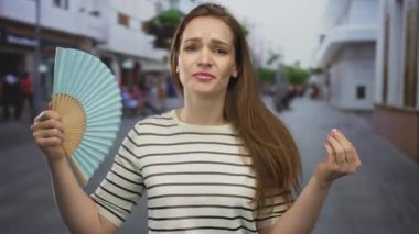 Kadın taraftarlar sıcak hava dalgası sırasında, kalabalık şehir caddesinde, kızgın öğle güneşi altında el bilgisayarı fanı ile karşı karşıya..