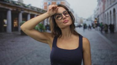 Gündüz vakti hareketli bir şehir caddesinde ter temizleyen bir kadın, gözlük takıyor ve kolsuz bluz giyiyor, omuzlarında görünür bir deri;.