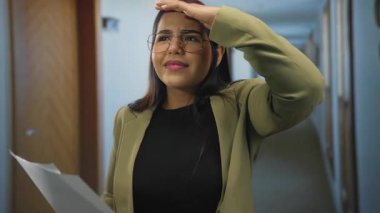 Bir otel koridorunda elinde gözlük ve spor ceket takmış bir gazete tutan bir kadın, evde merak ve keşifler yapıyor..