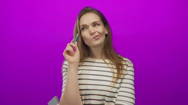 Mor stüdyoda dizüstü bilgisayarı tutan kadın çizgili gömlek giyiyor; düşünceli..