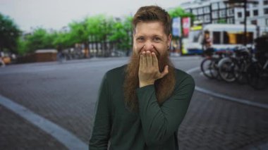 Yoğun caddede ağzı kapalı kırmızı sakallı bir adam bisiklet rafları ve tramvayla arka planda bekliyor. Sürpriz..