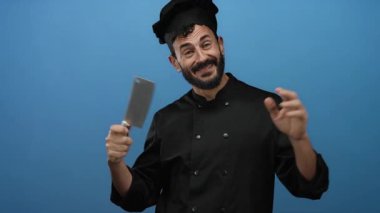 Sakallı İspanyol aşçı gülümsüyor ve mavi arka planda bir satırı tutuyor..