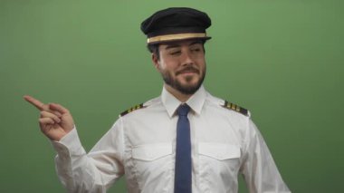 Sakallı, pilot üniformalı genç adam yeşil arka planda farklı yönlere bakıyor. Kendine güvenen ve düşünceli bir ifade sergiliyor..