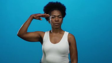 Mavi arka planda beyaz bluz giyen, güçlü pozlar veren bir kadın..