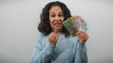 Orta yaşlı bir kadın, Avustralya dolarlarını gergin bir şekilde arka planda tutuyor. Duygusal bir mali endişe ve belirsizlik anını yakalıyor..