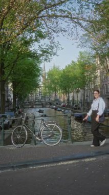 Güneşli gökyüzünün altında bisiklet süren, büyüleyici ağaçlar ve tarihi mimari ile çevrili, canlı şehir yaşam tarzını gözler önüne seren bir kadın..