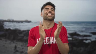 Gülümseyen sakallı İspanyol cankurtaran mavi gökyüzünün altında el çırpıyor..