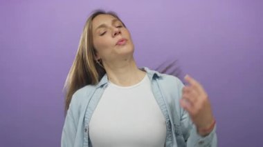 Sarışın genç bir kadın, izole edilmiş mor bir arkaplanda rahat bir şekilde poz veriyor. Günlük kıyafetler ve kot ceket giyiyor..