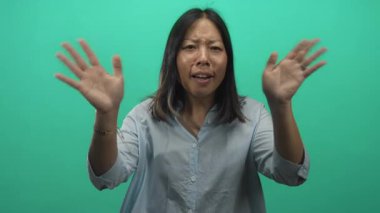 Stüdyoda elleri kameraya doğru yükselen, yeşil arkaplanı olan bir kadın; sürpriz bir dostça bağlantı enerjisi.