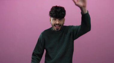 Pembe arka planda jest yapan genç adam yeşil süveter giyiyor canlı bir ifade ve tarz sergiliyor.