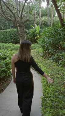 Yeşil yapraklı ve sakin atmosferli lüks bir tatil köyünde, yemyeşil tropik bahçe yolunda yürüyen bir kadın..