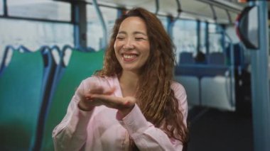 Kadın gülümseyen elleri açık sokak otobüsü koltuklarında pembe gömlekli, uzun saçlı, sevinç bağı sıcaklığında..