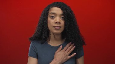 Ciddi ifadesi olan bir kadın elini göğsüne koydu ve diğer eli kırmızı stüdyo arkaplanına kaldırdı; samimiyet.