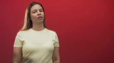 Genç bir kadın kollarını kavuşturuyor ve kırmızı stüdyo duvarına karşı elleri ve dilleriyle saygısız bir yüz ifadesi takınıyor..