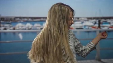 Parlak güneş ışığı altında teknelere tepeden bakan iskele binasında tırabzan öterek sarı saçlarını savuruyor. Mutluluk..