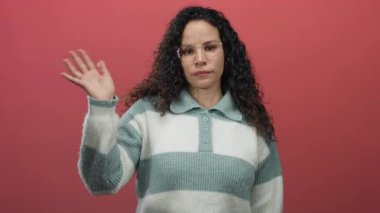 Gözlüklü, pembe arka planda sallanan, rahat çizgili süveter giyen, çeşitli duyguları ifade eden ve kameraya gelişigüzel poz veren bir kadın.