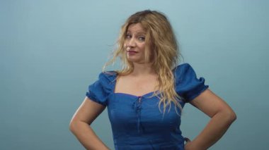 Stüdyoda göktaşı arkaplanlı, mavi elbiseli, dağınık sarı saçlı, onaylanmamış bir kadın var..