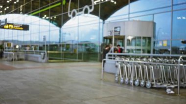 Havaalanı terminalindeki insanların puslu görüntüsü, tramvaylar ve modern bir cephe, yansımalar ve hareketlerle hareketli bir açık hava sahnesi..