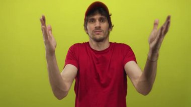 Geniş kolları ve çıplak elleri olan genç bir adam limon yeşili arka planı olan bir stüdyoda kırmızı başlık ve kırmızı gömlek giyiyor..