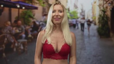 Kırmızı dantelli sutyen giyen bir kadın yaz güneşinde tententenin altında kaldırım taşı caddesinde bir sandık tutuyor..