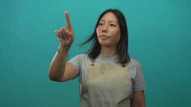 Stüdyoda önlük giyerken sol eliyle parmağını gösteren ve sağ eliyle işaret eden kadın, sabit bir bakış;.