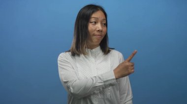 Mavi stüdyoda diğer kolunu göğsünden geçirip hafifçe omuz silkerken bir kadın sağı işaret ediyor..