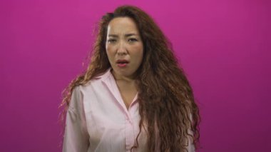 Kadın yüzü ve elleri pembe stüdyoda avuç içleriyle omuz silkiyor açık tişört ve uzun kıvırcık saçlar giyiyor; kayıtsız hareket.