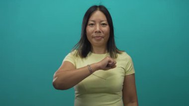 Kadın parmağı, sarı tişört ve bilezik giyen, sağ el ve ön kolda görünür bir şekilde kamerayı işaret ediyor..