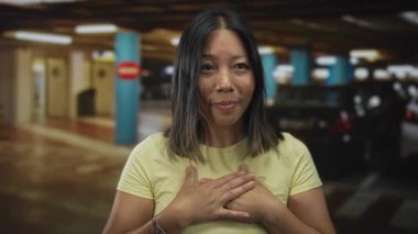 Kadın gözleri kapalı, elleri göğsünde, sarı gömlek, park halindeki arabaların yanında duruyor; huzur.