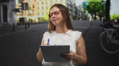 Kırmızı gözlüklü, işlek bir caddede elinde kalem ve pano tutan kadın, düşünceli bir planlama..