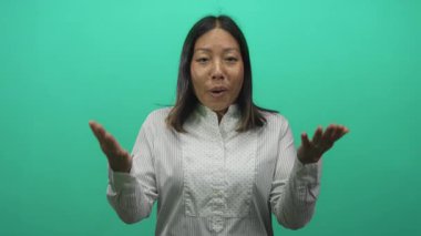 Elleri havada omuz silken genç bir kadın ve parlak yeşil stüdyo arka planında avuçlar görünür; sürpriz tepki jesti.