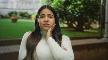 Dışarda, Sidikli Kule 'nin yanında kafası karışmış, yeşil arka planda beyaz bir kazak giyen bir kadın..