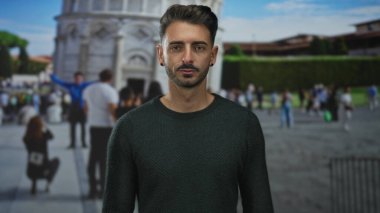 İspanyol asıllı genç adam, dışarıdaki pisa binasının tarihi eğimli kulesinin önünde poz veriyor..