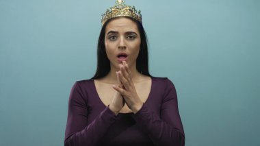 Altın taç giyen İspanyol kadın mavi duvara karşı poz veriyor gergin ama asil bir ifade sergiliyor elleri bağlı, özgüven ve zarafet sergiliyor.