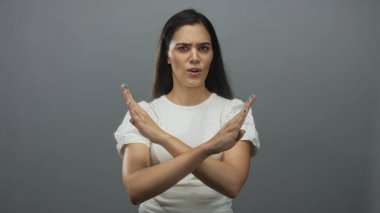 Gri stüdyoda, çatık kaşlı, aralıklı dudaklı ve doğrudan bakışlı kadın ellerini sıkıca çaprazlar..