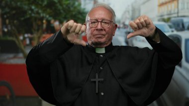 Siyah cüppeli kıdemli rahip, şehir yaşamını tasvir eden resmi bir ifadeyle sokak ortasında dikiliyor..