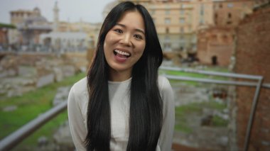 Roma harabelerine gülümseyen uzun saçlı genç bir kadın, tarihi bir zemine karşı neşeli bir enerji yayıyor..