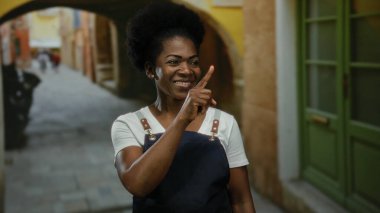 Önlük takan bir kadın canlı bir şehir caddesinde dikilirken, açık hava yaşamını yansıtıyor..