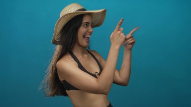 Mavi stüdyoda hasır şapka takan genç İspanyol kadın, heyecan ve merak..