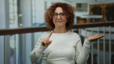 Otelde parmak ve avuç içi açık el kol hareketi yapan bir kadın, kapalı alanda belirsizlik olduğunu gösteriyor..