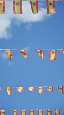 İspanya 'da güneşli bir günde açık mavi gökyüzünde dalgalanan renkli İspanyol bayrakları şenlikli ve canlı bir atmosferi simgeliyor..